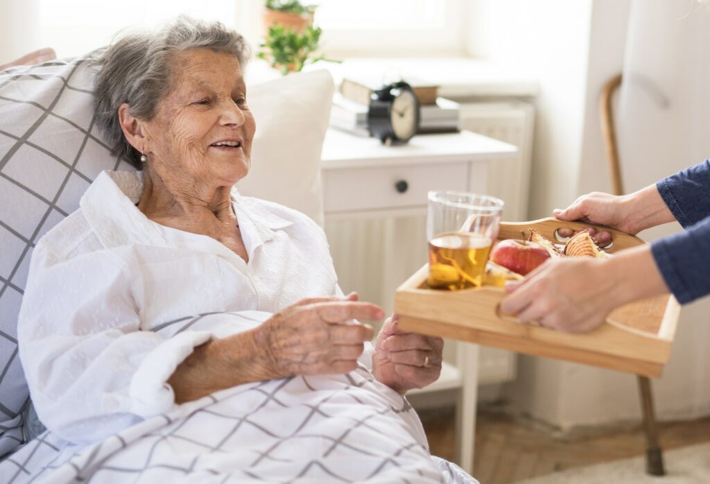 Elderly woman in bed being handed a tray of food